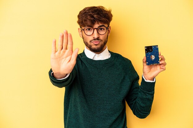 Jonge computerizer man geïsoleerd op gele achtergrond permanent met uitgestrekte hand weergegeven: stopbord, voorkomen dat u.