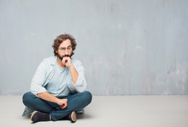 Jonge cool bebaarde man zittend op de vloer. grunge muur achtergrond