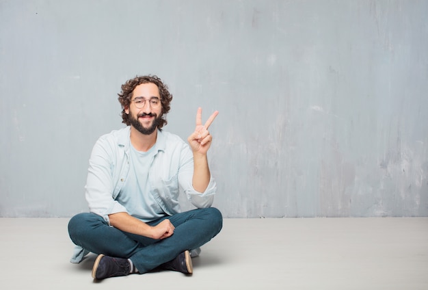 Jonge cool bebaarde man zittend op de vloer. grunge muur achtergrond