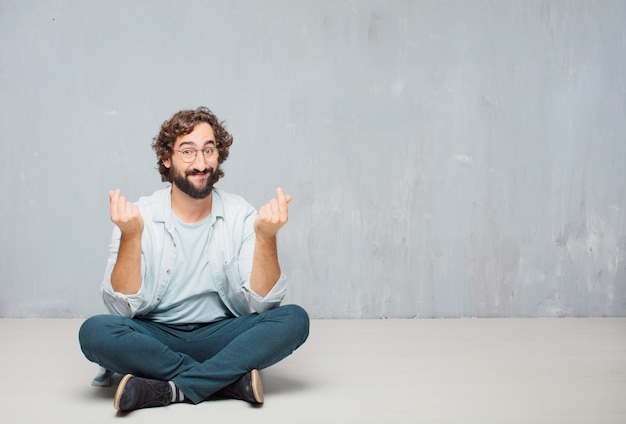 Jonge cool bebaarde man zittend op de vloer. grunge muur achtergrond