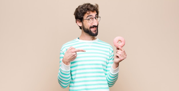 Jonge cool man met een suiker roze donut tegen vlakke muur