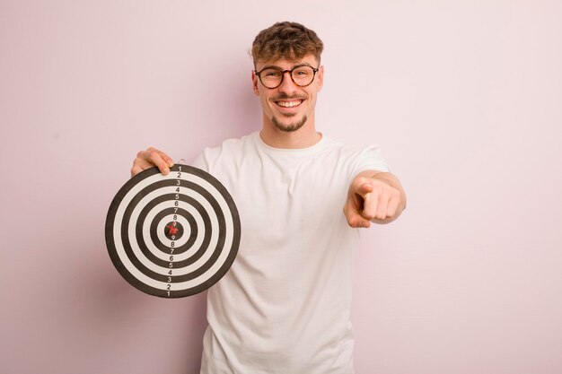 Jonge coole man die naar de camera wijst en je dartdoelconcept kiest