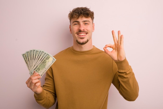 Jonge coole man die zich gelukkig voelt met goedkeuring met een goed gebaar dollarbankbiljettenconcept