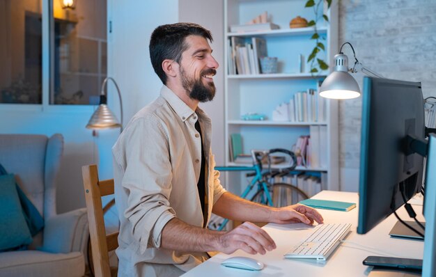 Jonge creatieve ondernemer die gelukkig glimlacht terwijl hij thuis in zijn moderne werkruimte werkt