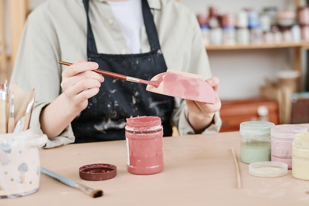 Jonge creatieve vrouw in schort met penseel en kleikom boven tafel