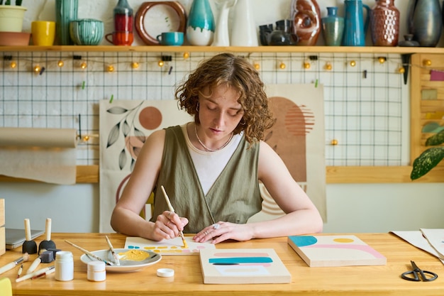 Jonge creatieve vrouw in vrijetijdskleding die nieuw schilderij maakt door werkplek in studio