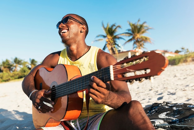 Jonge Cubaanse man die plezier heeft op het strand met zijn gitaar. Vriendschapsconcept.