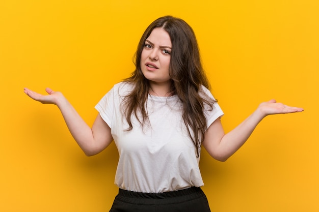 Jonge curvy plus groottevrouw verward en twijfelachtig die hem opheft om een exemplaarruimte te houden.