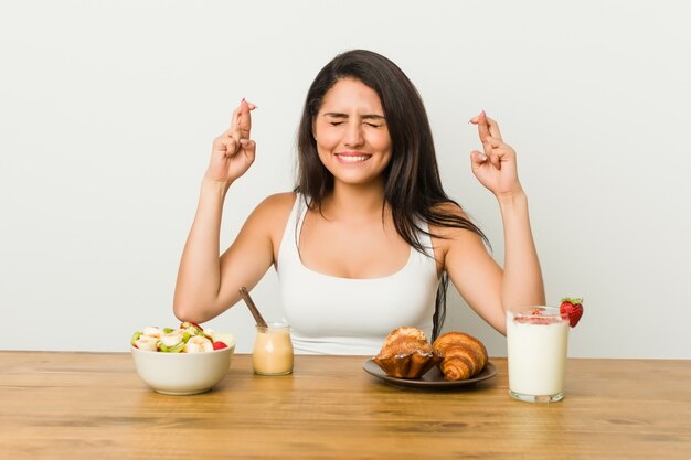 Jonge curvy vrouw die een ontbijt neemt dat vingers kruist voor het hebben van geluk