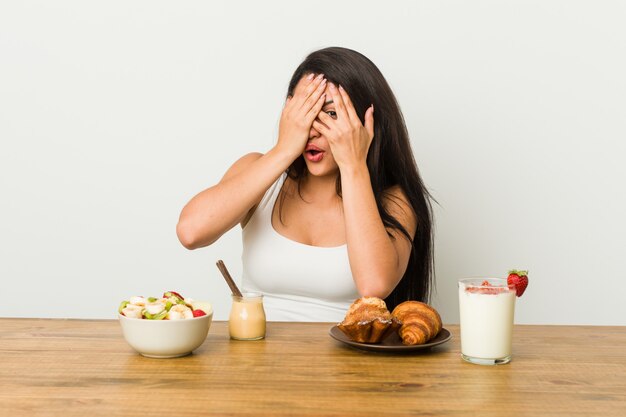 Jonge curvy vrouw die een ontbijt neemt knipoogt door angstig en zenuwachtige vingers.