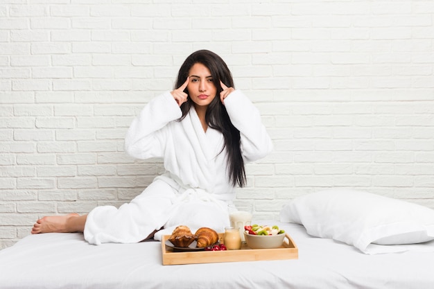 Jonge curvy vrouw die een ontbijt op het bed nam concentreerde zich op een taak, houdend wijsvingers die hoofd richten.