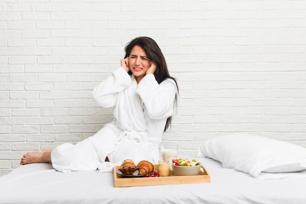 Jonge curvy vrouw die een ontbijt op het bed neemt dat oren behandelt met handen.