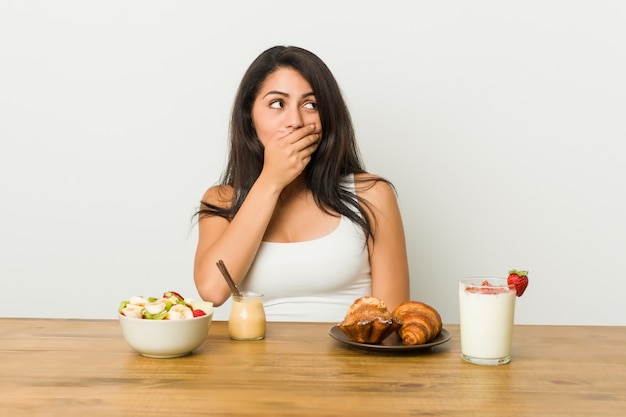 Jonge curvy vrouw die ontbijt het nadenkende kijken nemen aan een exemplaarruimte die mond behandelen met hand.