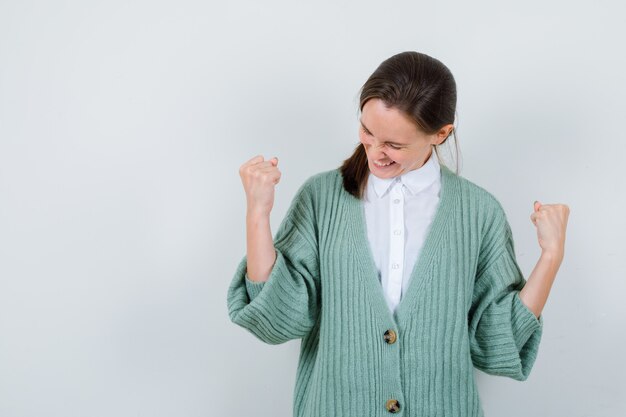Jonge dame die winnaargebaar in blouse, vest toont en vrolijk kijkt. vooraanzicht.