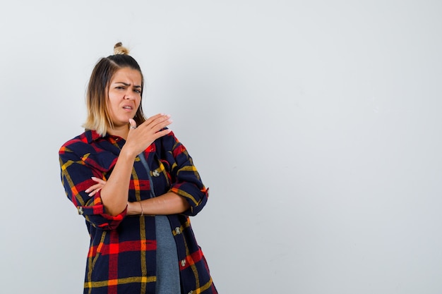 Jonge dame in casual geruit hemd die hand voor haar opsteekt en er ontevreden uitziet, vooraanzicht.