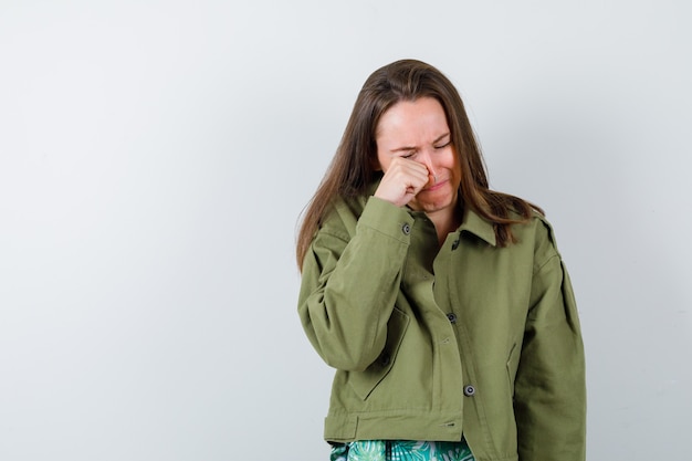 Jonge dame in groene jas die in de ogen wrijft terwijl ze huilt en er depressief uitziet, vooraanzicht.