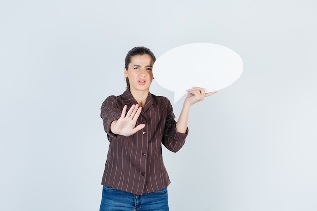 Jonge dame in shirt, spijkerbroek met stopgebaar, papieren poster bijgehouden en teleurgesteld, vooraanzicht.