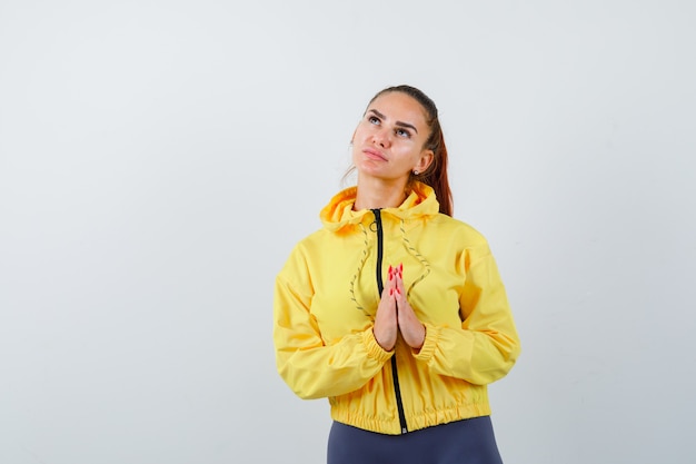 Jonge dame in trainingspak met namaste-gebaar terwijl ze opkijkt en er hoopvol uitziet, vooraanzicht.