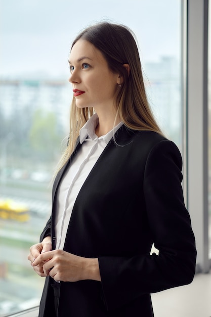 Jonge dame in wit overhemd en zwarte jas die zich bij het raam bevindt