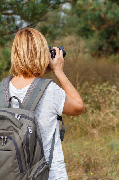 Jonge dame loopt door in het bos met digitale camera. Wandelaar met rugzak die foto's maakt van het zomerlandschap buiten in de natuur. Gezonde actieve levensstijl