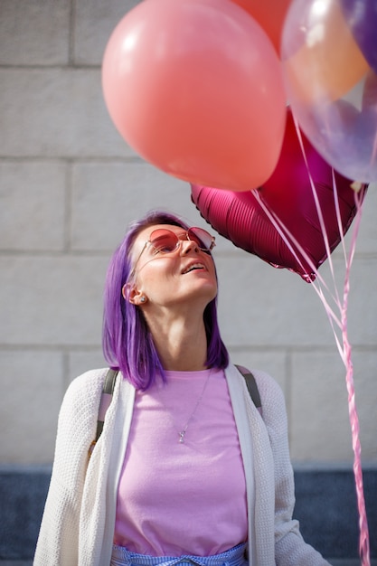 Foto jonge dame met violet haar in glazen met omhoog en ballons die kijken glimlachen