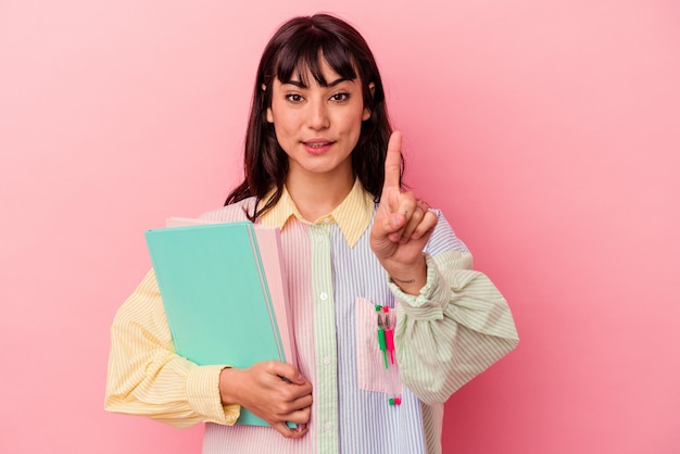 Jonge de holdingsboeken van de studenten Kaukasische vrouw die op roze muur worden geïsoleerd die nummer één met vinger toont.