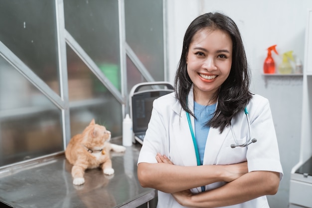 Jonge dierenarts glimlachend met gekruiste handen in de buurt van een kat zit op de tafel bij de dierenartskliniek