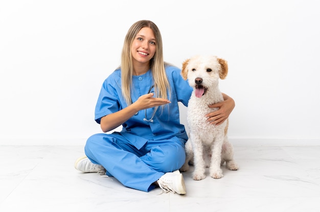 Jonge dierenarts vrouw met hond zittend op de vloer handen uitstrekkende naar de zijkant om uit te nodigen om te komen