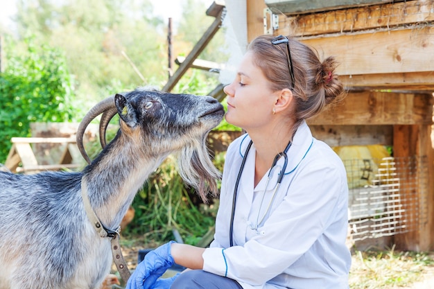 Jonge dierenartsvrouw die met stethoscoop geit op ranch houdt en onderzoekt