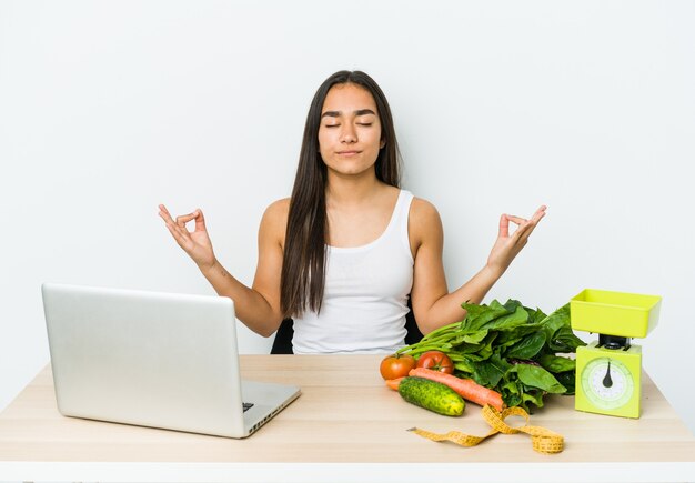 Jonge diëtist Aziatische vrouw geïsoleerd op een witte muur ontspant na een zware werkdag, ze voert yoga uit.