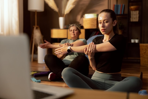 Foto jonge dochter met bejaarde moeder die samen tijd doorbrengt zittend op yogamat in lotushouding