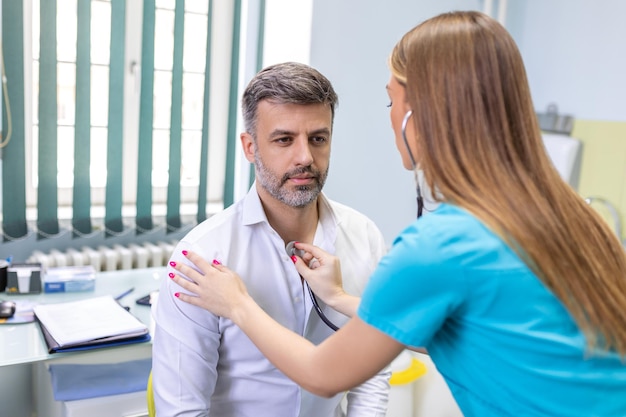 Jonge dokter gebruikt een stethoscoop luister naar de hartslag van de patiënt Shot van een vrouwelijke arts die een mannelijke patiënt een check-up geeft