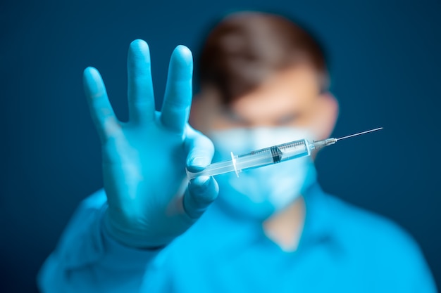 Jonge dokter met een blauw masker houdt een injectiespuit voor zich