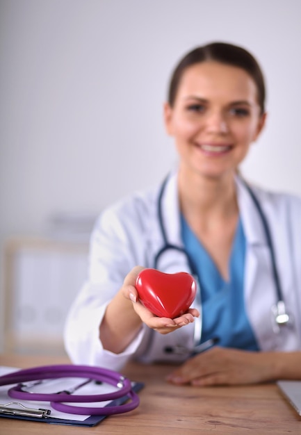 Jonge dokter met rood hartsymbool zit aan bureau geïsoleerd