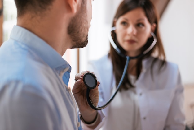 Foto jonge dokter onderzoekt de patiënt met een stethoscoop.