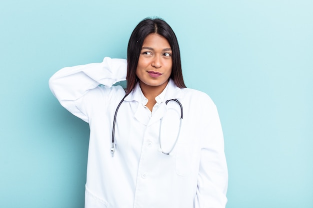 Jonge dokter venezolaanse vrouw geïsoleerd op blauwe achtergrond achterhoofd aanraken, denken en een keuze maken.