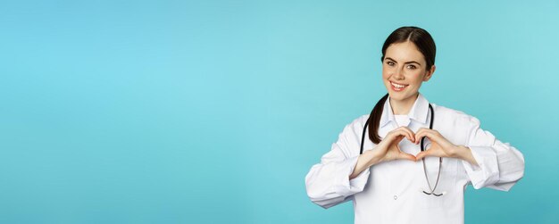 Jonge dokter vrouw arts die hart liefde teken toont en glimlachende zorg voor patiënten in kliniek standin