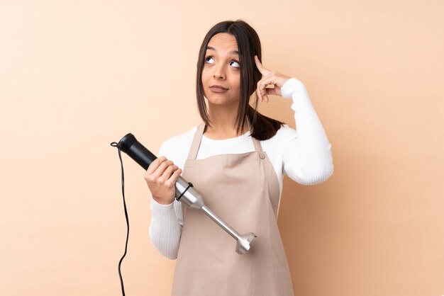 Jonge donkerbruine jonge vrouw die geïsoleerde handmixer met behulp van