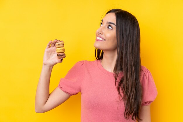 Jonge donkerbruine kleurrijke macarons houden en vrouw die omhoog terwijl het glimlachen kijken