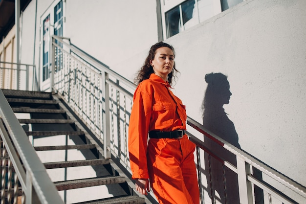 Jonge donkerbruine krullende vrouw in oranje kostuum. Wijfje in kleurrijk overallportret.