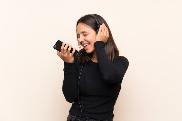 Jonge donkerbruine meisje het luisteren muziek met mobiel over geïsoleerde muur