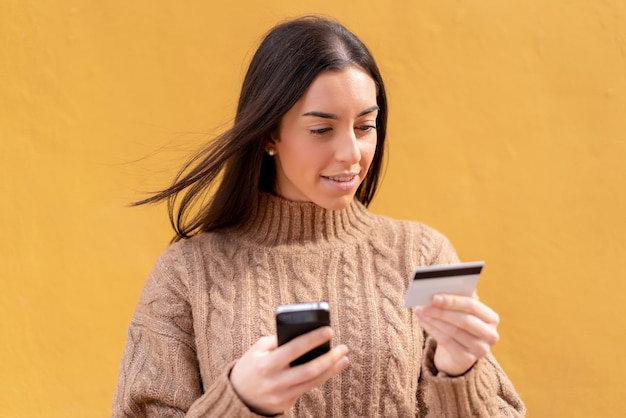 Jonge donkerbruine vrouw die buitenshuis koopt met de mobiel met een creditcard