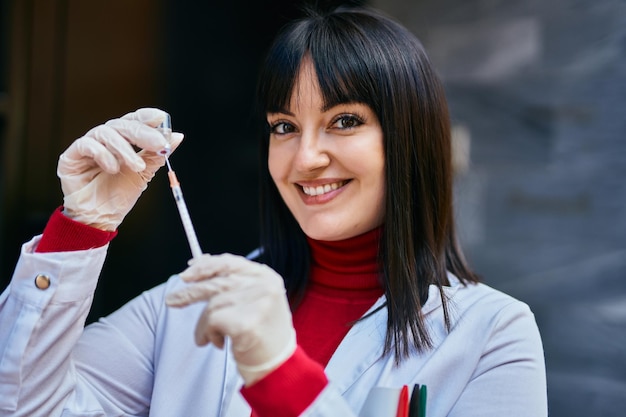 Jonge donkerbruine vrouw die een artsenuniform draagt met spuit en vaccin in de stad