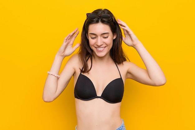 Jonge donkerbruine vrouw die een bikini draagt tegen gele muur blij veel lachen