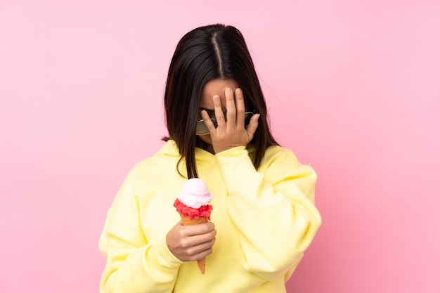 Jonge donkerbruine vrouw die een cornetroomijs over geïsoleerde roze muur met vermoeide en zieke uitdrukking houdt