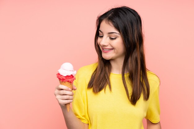 Jonge donkerbruine vrouw die een cornetroomijs over roze muur met gelukkige uitdrukking houdt