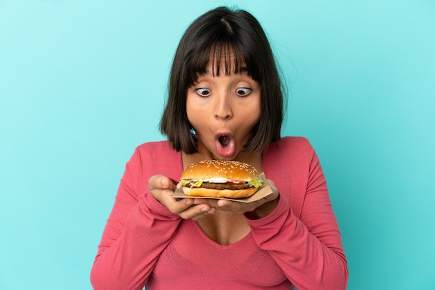 Jonge donkerbruine vrouw die een hamburger over geïsoleerde achtergrond houdt
