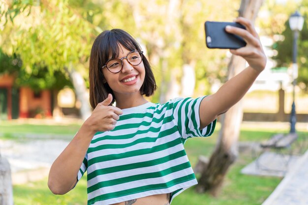 Jonge donkerbruine vrouw in het park die een selfie met mobiele telefoon maakt