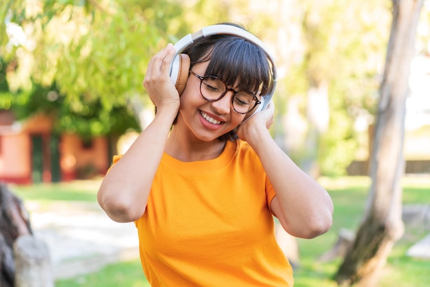 Jonge donkerbruine vrouw in het park die muziek luistert