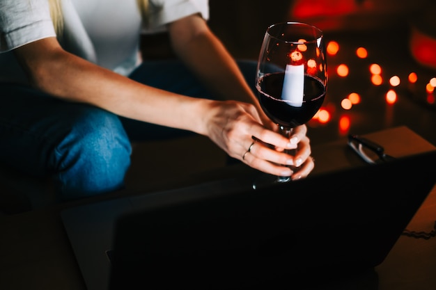 Jonge duizendjarige vrouw die videogesprek heeft op een laptop en wijn drinkt, gebruikt technologie om te communiceren met vrienden of familie.